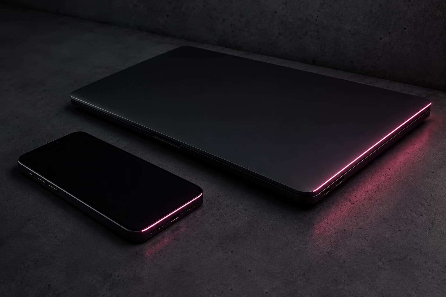 A sleek matte-black laptop and phone lit by a single line of pink light